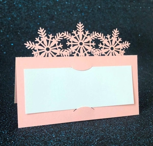 Pink laser-cut snowflake place card with white insert on blue glitter background