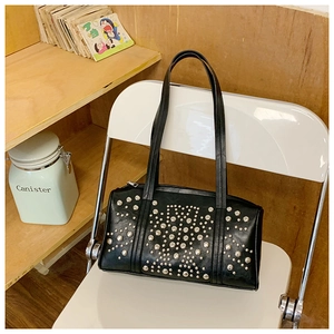 Detail of silver rivets on black leather shoulder bag placed on a white chair