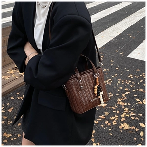 Gros plan d'un sac seau tressé marron foncé avec charm perlé et détails en métal poli