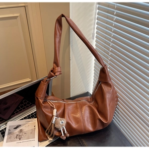 Detail of a brown leather dumpling bag featuring soft pleats and a decorative bear charm