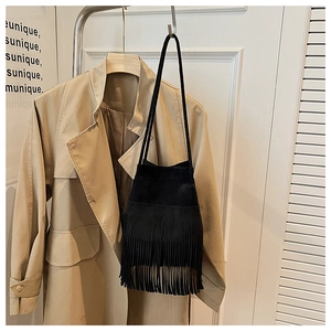 Detail shot of a black suede bucket bag with long fringe tassels on an overcoat background