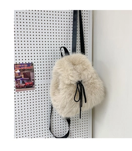 Close-up of cream plush backpack featuring black drawstring bow and adjustable straps