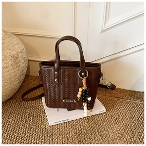 Gros plan d'un sac seau tressé marron foncé avec logo métallique et pendentif perlé