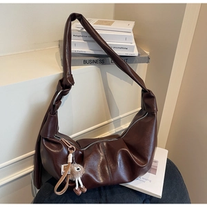 Detail of dark brown hobo bag featuring knotted leather strap and plush doll pendant