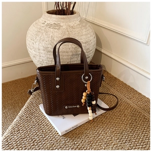 Détail du sac cabas tressé marron foncé avec plaque logo et breloque en perles chic