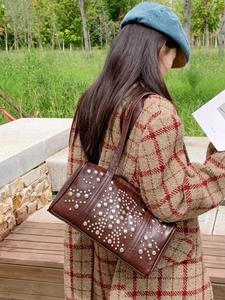 Brown vintage leather shoulder bag with silver rivets worn over a plaid coat