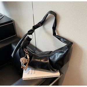 Detail of black leather hobo bag featuring a knotted strap and plush bear charm accent