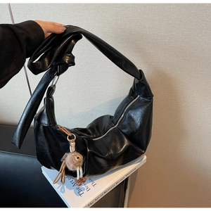 Detail of black glossy PU leather crescent bag with wide strap and plush pendant