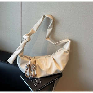 Close-up of cream half-moon shoulder bag with glossy leather, knot strap and bear charm