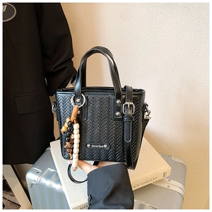 Détail du sac à main noir tressé avec breloque en perles posé sur une valise argentée