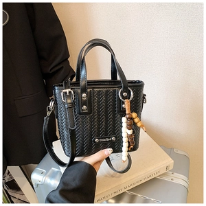 Détail de la texture tressée du sac noir avec breloque en bois et plaque en métal gravée