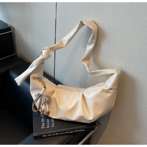 Detail view of off-white pleated dumpling bag with knotted strap and plush monster charm