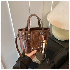 Détail du sac à main marron à texture tressée avec breloque perlée et fermoir argenté