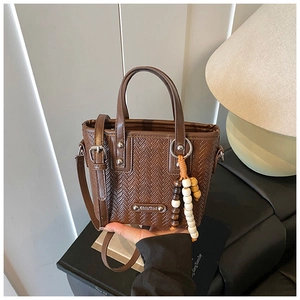 Détail d'un sac à main marron à texture tressée avec breloque perlée et plaque logo