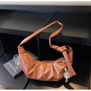 Detailed view of brown ruched crescent bag with knotted strap and plush charm accent