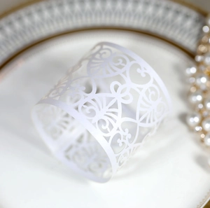 Detail of laser-cut white paper napkin ring with intricate floral vine pattern on a plate