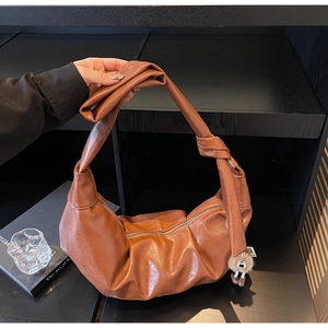 Detail of a brown hobo bag with knotted wide strap and plush pom-pom charm on shelf