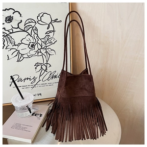 Detail view of dark brown suede bucket bag with long fringe tassels on a metal table