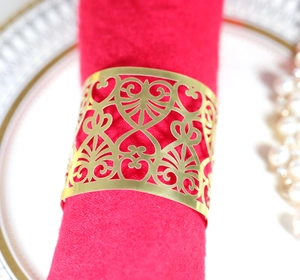 Macro detail of gold laser-cut heart pattern napkin ring on a red cloth napkin