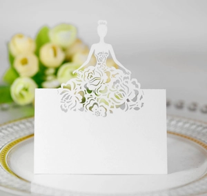 Detail of laser-cut white place card with floral dress silhouette on white porcelain plate