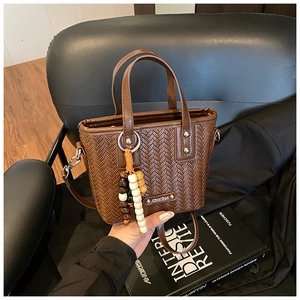 Détail d'un sac cabas en cuir tressé marron avec pendentif en bois sur un fauteuil