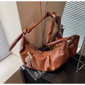 Detail of soft brown leather crescent bag showing trendy knotted strap and zip pompom