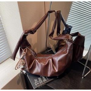 Detailed shot of dark brown glossy croissant bag with knotted strap and tassel charm