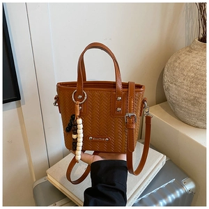 Détail d'un sac à main marron à texture tressée avec breloque en perles et bandoulière
