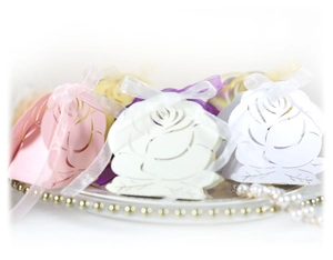 Laser cut rose hollow wedding candy box with ribbon bow in assorted colors on a plate