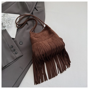 Detail of a brown suede shoulder bag featuring long fringe tassels and a bohemian style