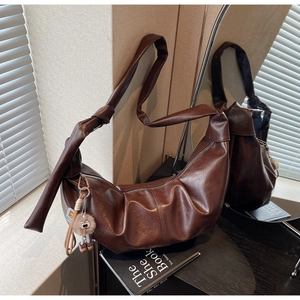 Detail of dark coffee ruched crescent bag with glossy texture and plush charm