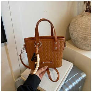 Détail du sac seau en cuir tressé marron avec breloque perlée sur des livres blancs