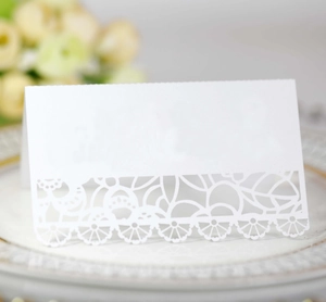 Detail view of laser-cut white lace place card on elegant dinner plate for weddings