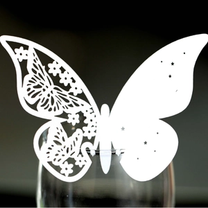 Elegant white laser-cut butterfly place card clipped onto a glass rim for events