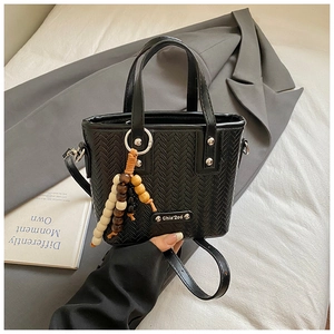 Détail du sac seau tressé noir avec pompon en perles et logo métallique sur fond élégant
