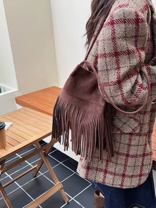 Dark brown suede bucket bag with long tassels shown on shoulder in outdoor cafe setting