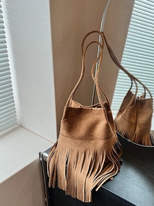Brown faux suede bucket bag with long tassels and shoulder strap in a minimalist setting