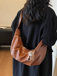 Brown leather moon shoulder bag with fluffy charm shown on a model in a long black coat