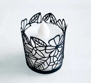 Detail of black laser-cut paper tea light sleeve with floral pattern and LED candle