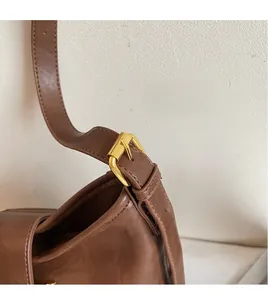 Detail of adjustable long brown leather strap and polished gold metal buckle on shoulder bag