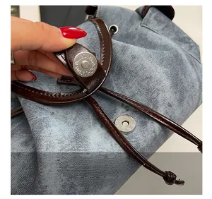 Détail du fermoir magnétique rond et couture en cuir marron sur le sac en jean