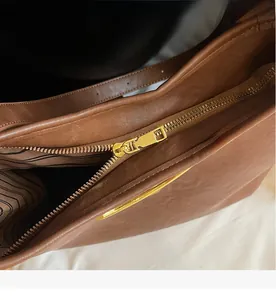 Detail of smooth gold zipper closure and striped fabric lining on a brown leather bag