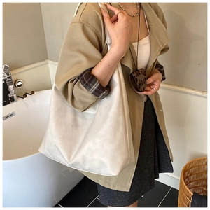 Detail of a large cream faux leather tote bag worn by a model in a minimalist setting