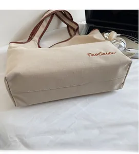 Detail of canvas tote bag with brown leather trim and TaoCaitu embroidered logo