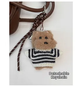 Close-up of a brown teddy bear charm with a striped sweater on a leather handbag