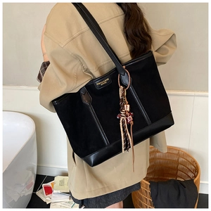 Detail of black tote bag featuring matte suede texture and ethnic tassel charm