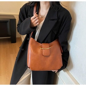 Detail view of caramel brown commuter tote featuring arched gold metal trim and matte finish