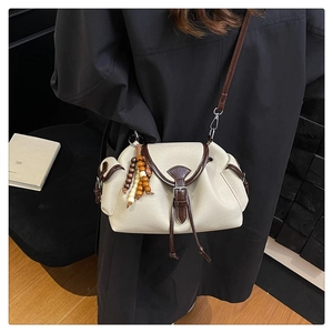 Dettaglio borsa a tracolla in tela beige con finiture in pelle marrone e ciondolo in legno