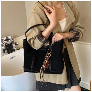 Detail of black suede and leather tote bag featuring colorful fringe charm accessory