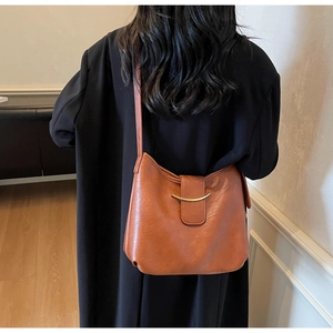 Detail of a brown tote bag with a golden horn-shaped buckle on a black coat